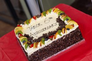 Square cake with chocolate on the sides, fruit around top edge and Tabor 6th anniversary written in chocolate on white icing